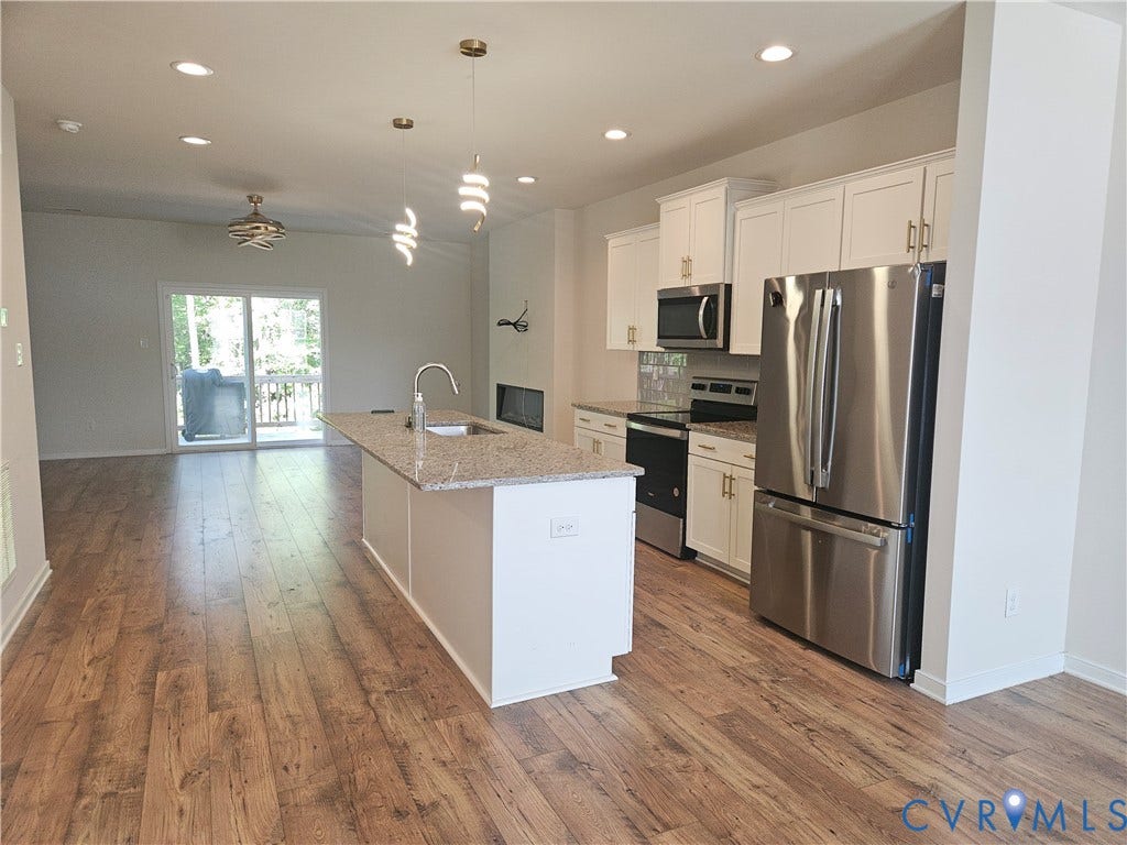 11304 Magill Terrace Drive, Chester, VA 23831 Open-concept kitchen and dining area featuring a large center island with granite countertop, stainless steel appliances including a French-door refrigerator and built-in microwave, white cabinetry, recessed lighting, and wood-finish flooring throughout the space