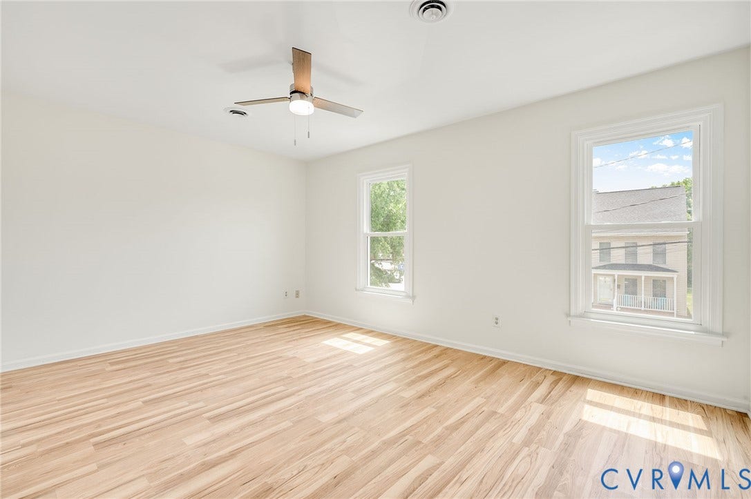 1723 Porter Street, Richmond, VA 23224 Spacious room featuring light wood-finish flooring, two large windows with white trim, a ceiling fan with integrated lighting, and white painted walls