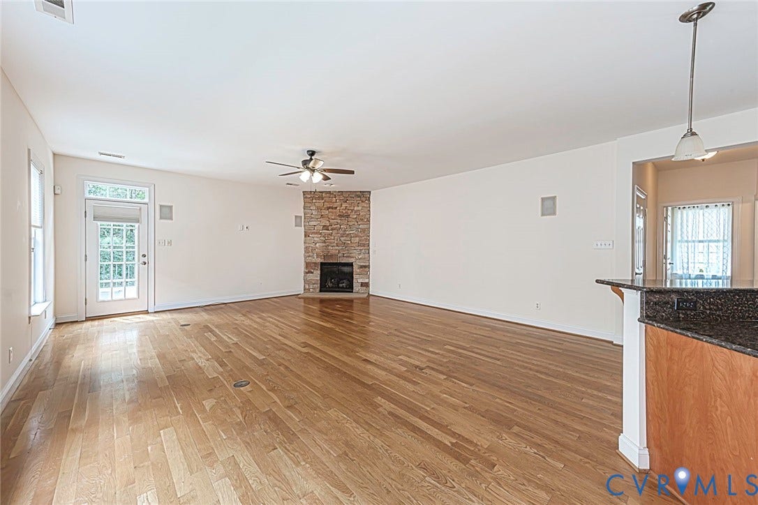 4309 Village Creek Drive, Chester, VA 23831 Spacious living area featuring wood-finish flooring, a stone-faced fireplace, and a ceiling fan, open to kitchen. Rear back door to rear deck.