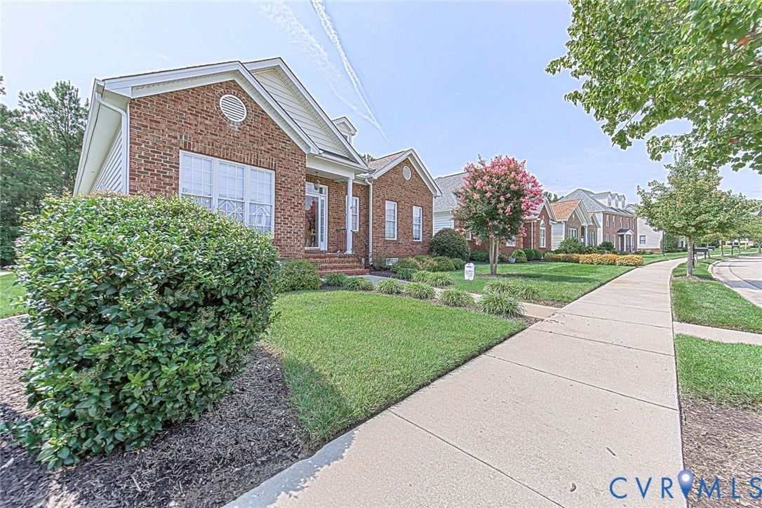 4309 Village Creek Drive, Chester, VA 23831 Traditional brick facade featuring white gables, a covered front porch with white columns, and a landscaped front yard with mature shrubbery and a manicured lawn. Chester Village has sidewalks, street lights.