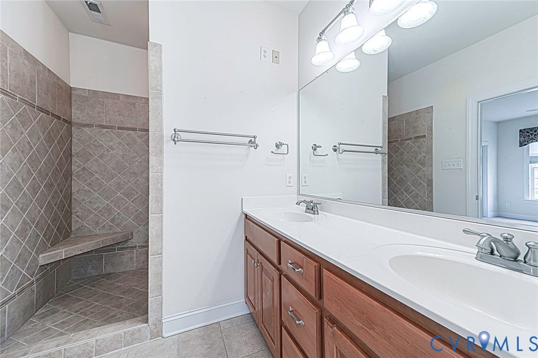 4309 Village Creek Drive, Chester, VA 23831 Primary bathroom featuring a dual vanity with white marble countertops, custom wood cabinetry, large ceramic tile shower with seat and chrome fixtures, ceramic tile flooring