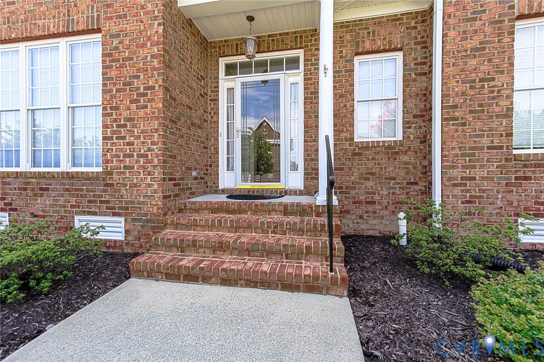 4309 Village Creek Drive, Chester, VA 23831 Brick front and brick rear exterior with multiple white-framed windows, a glass-paneled entry door, and a covered porch