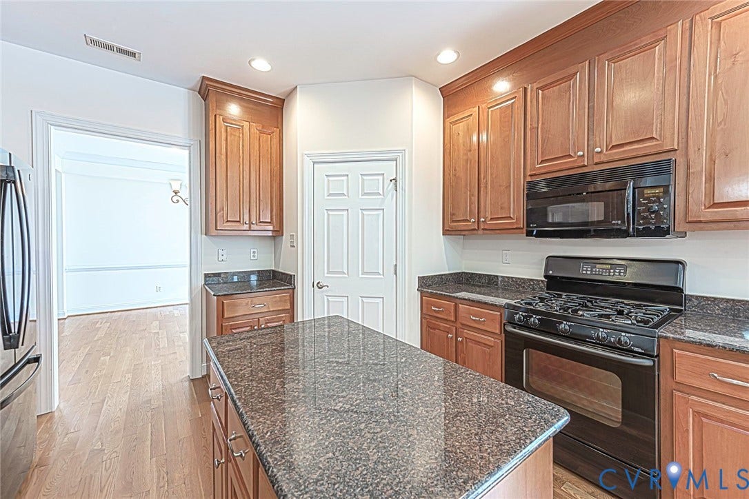 4309 Village Creek Drive, Chester, VA 23831 Kitchen featuring a central island with granite countertops, wood-finish flooring, recessed lighting, wood custom cabinetry, and a black gas range with an overhead microwave, stainless steel refrigerator and large pantry, recess lighting.