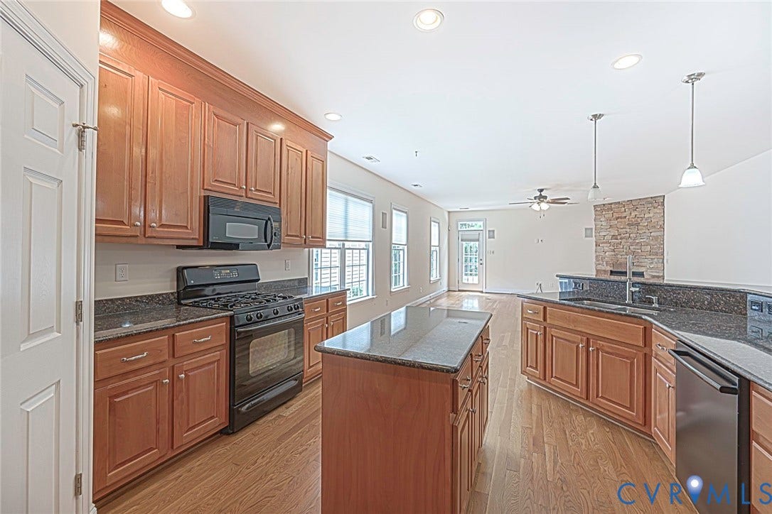 4309 Village Creek Drive, Chester, VA 23831 Open-concept kitchen featuring wood-finish cabinetry, dark stone countertops, a central island, and black appliances. Overlooking family room. Eat in area