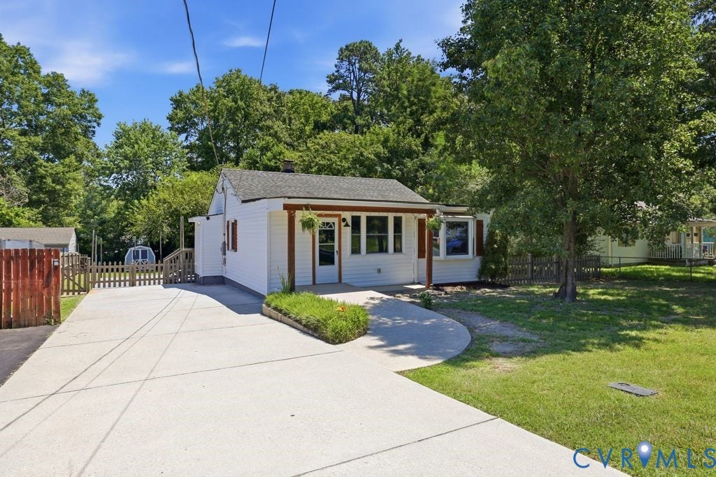 White siding exterior with a dark shingle roof, a covered entry porch, and red window shutters
