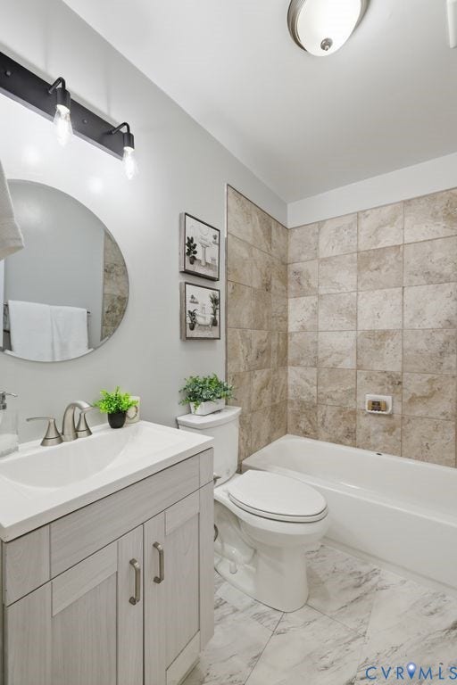 Bathroom featuring a light-toned vanity with a white countertop and brushed nickel hardware, a circular mirror, a toilet, a white bathtub, and floor-to-ceiling tile surrounding the tub