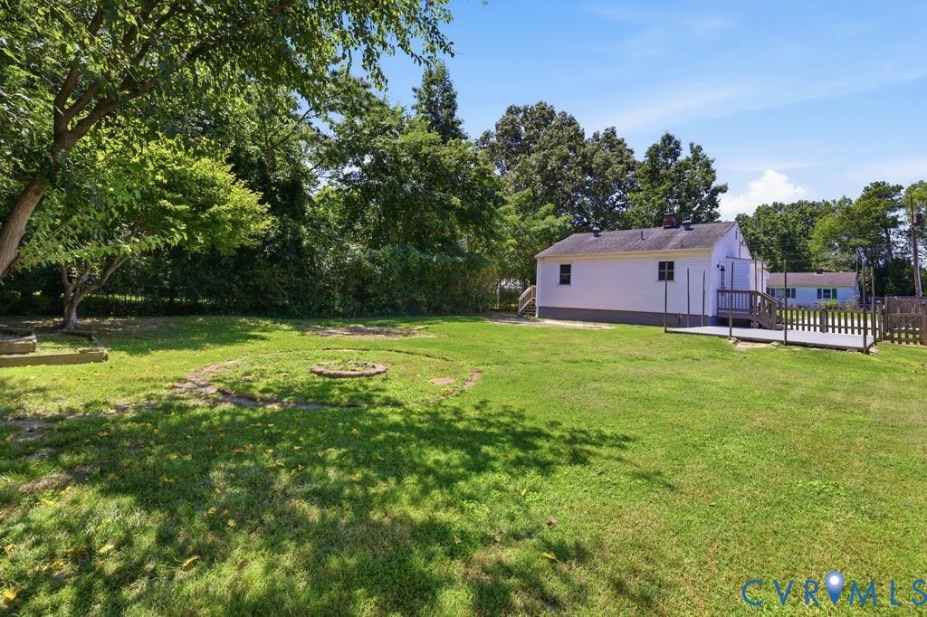 Expansive rear yard featuring a large wooden deck, mature trees, and a wooden privacy fence