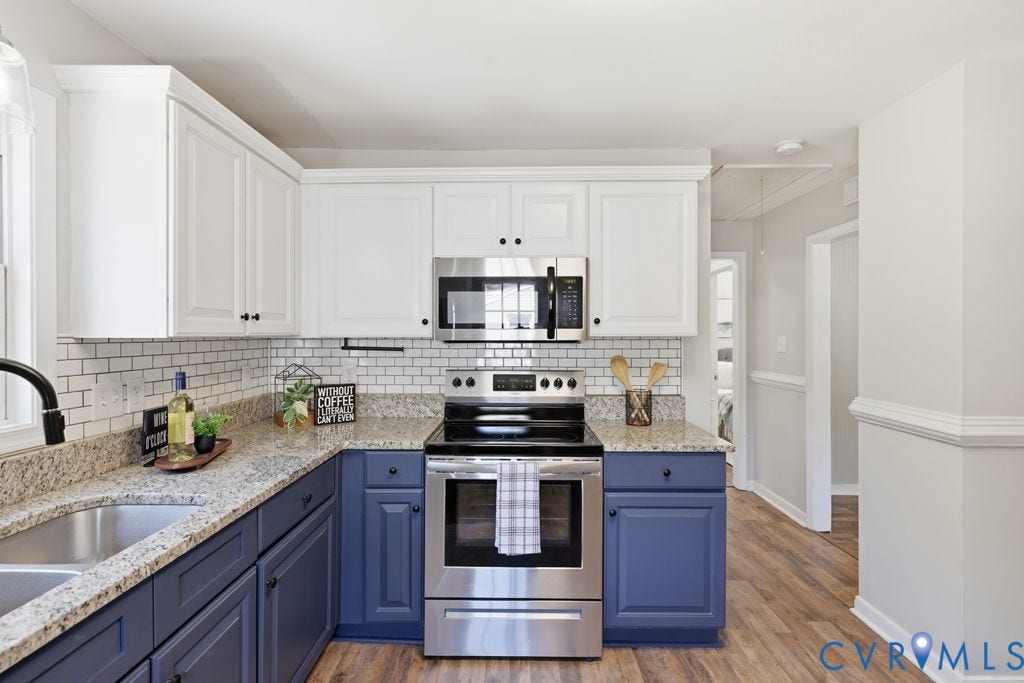 Kitchen featuring white upper cabinetry, blue lower cabinetry, stainless steel appliances, granite countertops, and subway tile backsplash