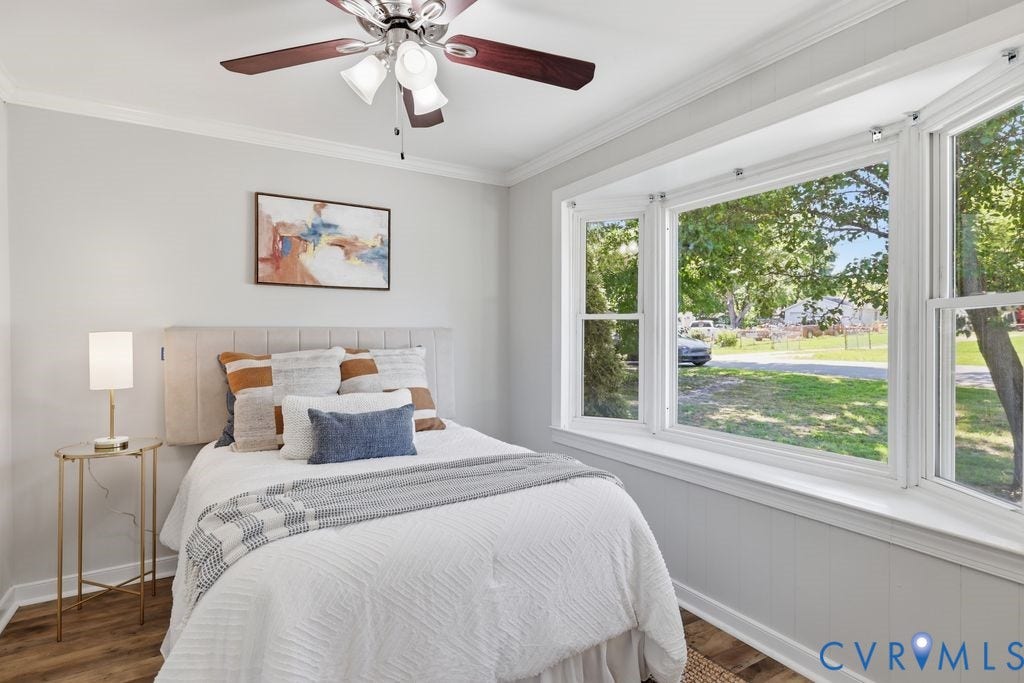 Bedroom featuring a multi-pane bay window, wood-finish flooring, a ceiling fan with integrated lighting, and crown molding