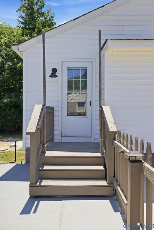 Rear entry with wood steps and railings, featuring a glass-paneled door and exterior wall sconce