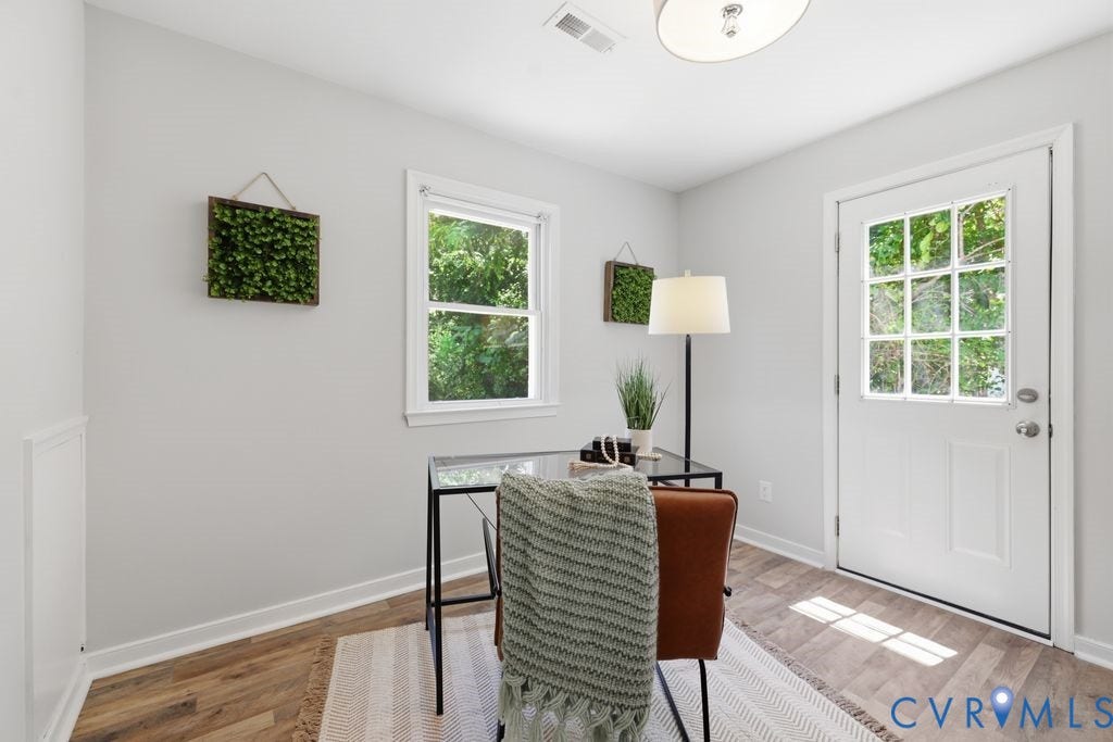 Bright interior space featuring a window with exterior views, a white paneled door with glass inserts, wood-finish flooring, and white baseboards