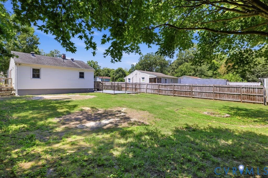 Spacious backyard featuring a wooden privacy fence, expansive green lawn, and a ground-level deck