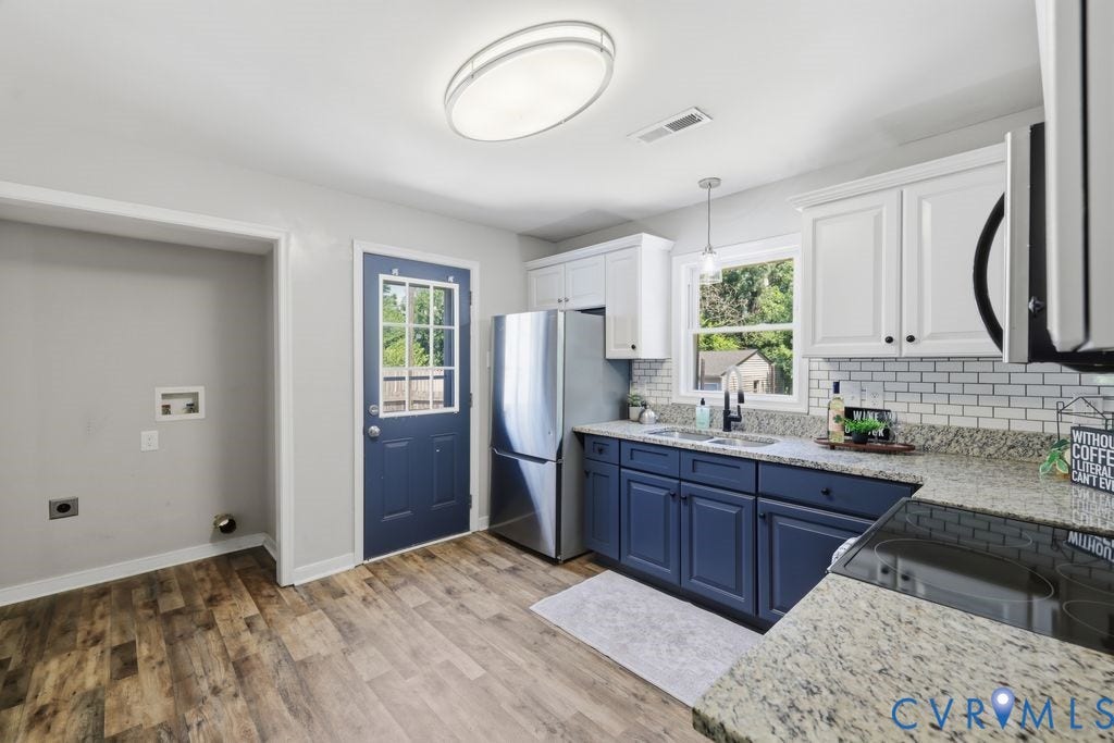Kitchen featuring wood-finish flooring, two-tone cabinetry with white upper and blue lower cabinets, light-toned granite countertops, and a subway tile backsplash