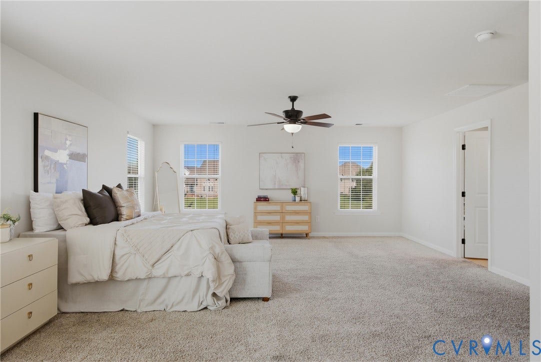 1819 White Mountain Drive, Mount Blanco On The James, Chester, VA 23836 Spacious bedroom featuring plush carpet flooring, two large windows with horizontal blinds, and a dark-toned ceiling fan with integrated lighting