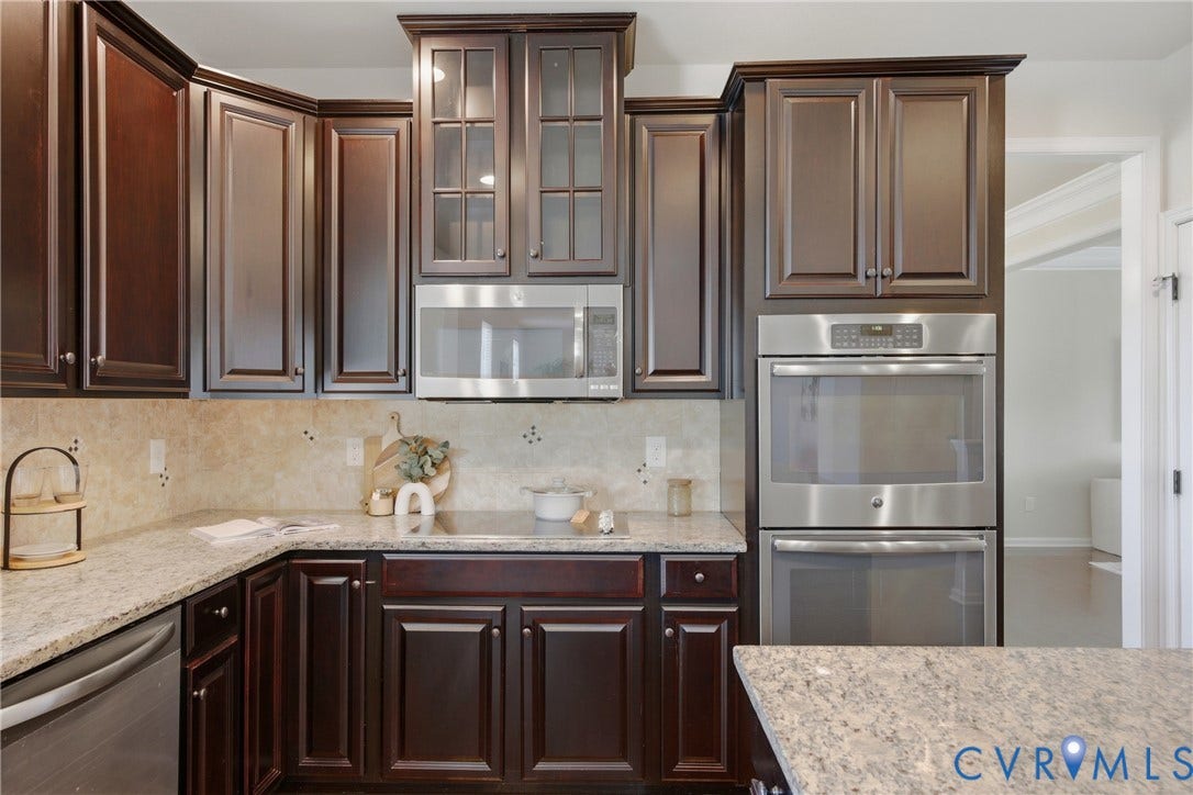 1819 White Mountain Drive, Mount Blanco On The James, Chester, VA 23836 Kitchen featuring dark wood cabinetry with crown molding, light-toned granite countertops, a tiled backsplash, stainless steel microwave, and double wall ovens