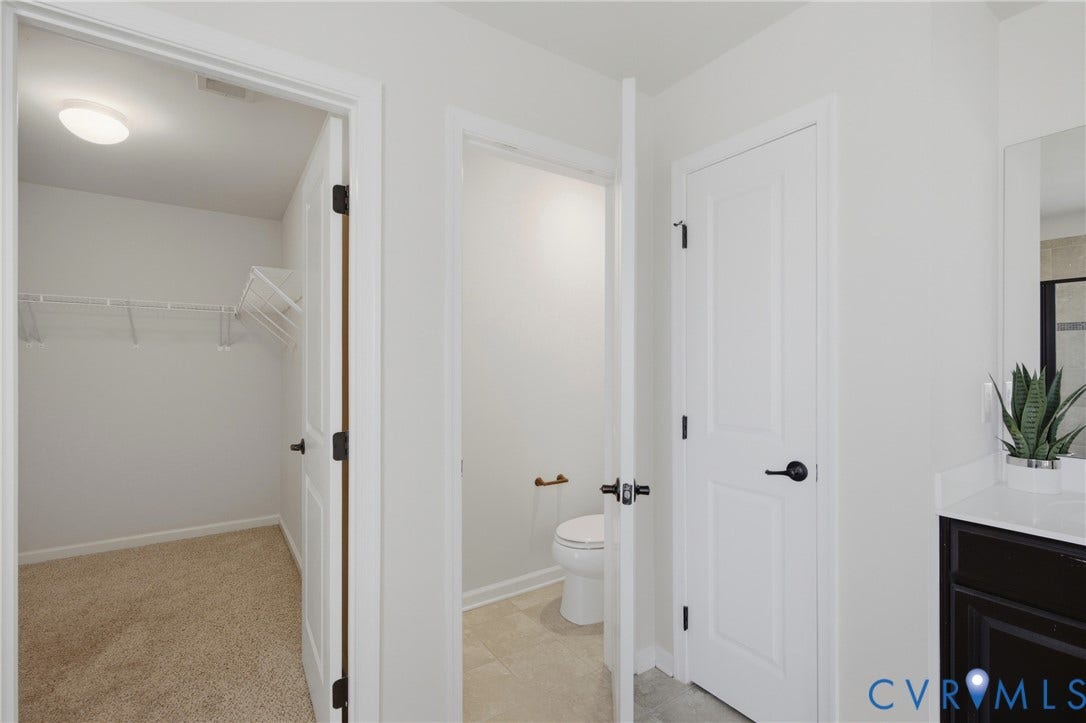 1819 White Mountain Drive, Mount Blanco On The James, Chester, VA 23836 Bathroom interior featuring a dark wood-finish vanity with a white countertop, a white toilet, and a separate carpeted closet with wire shelving