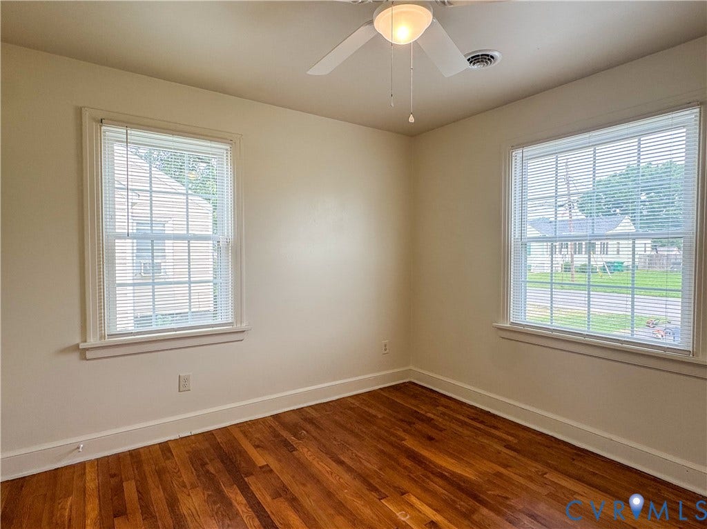Room featuring wood-finish flooring, two large windows with blinds, a ceiling fan with integrated lighting, white trim, and neutral wall paint