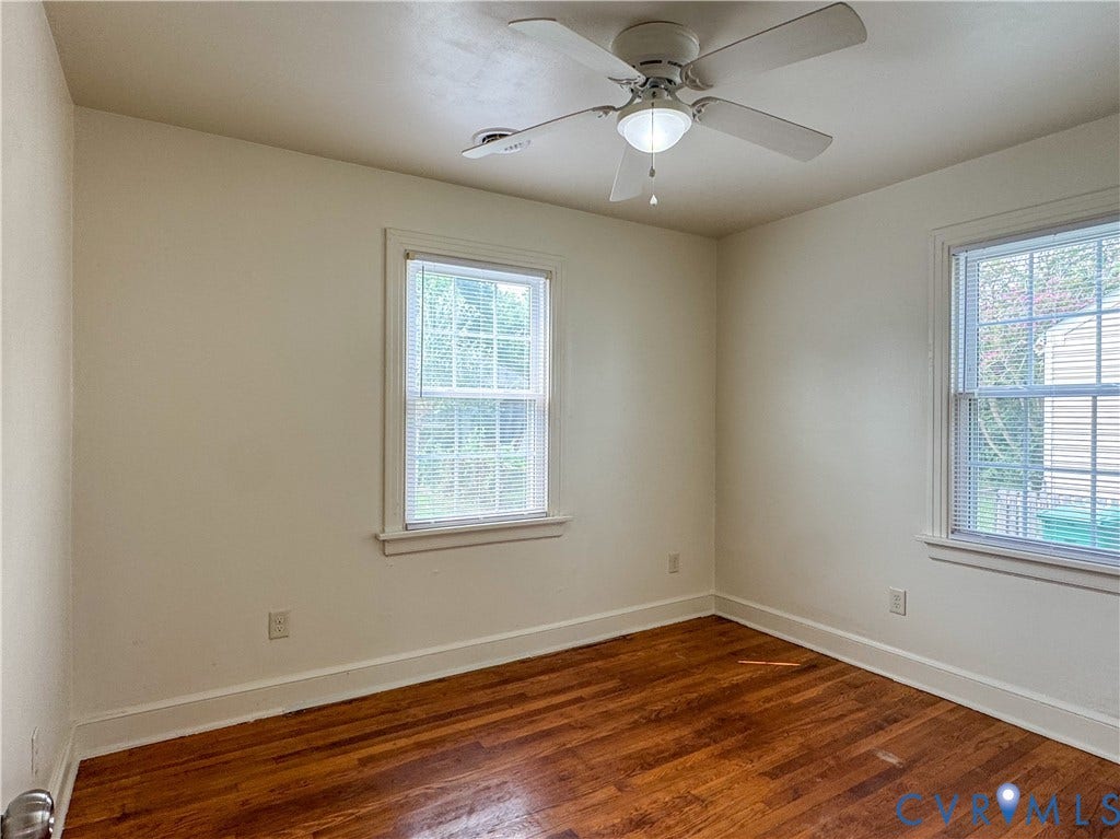 Interior room featuring rich wood-finish flooring, two window openings, a ceiling fan with integrated lighting, white baseboards, and white window trim