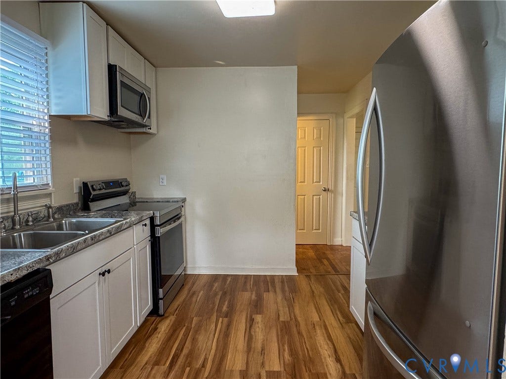 Kitchen featuring wood-finish flooring, white cabinetry, a stainless steel refrigerator, and a double basin sink