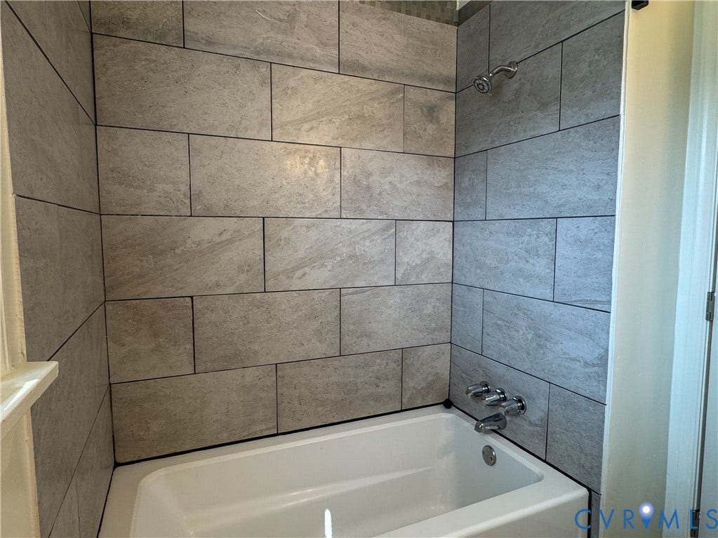 White bathtub with chrome fixtures, surrounded by light gray, rectangular wall tiles