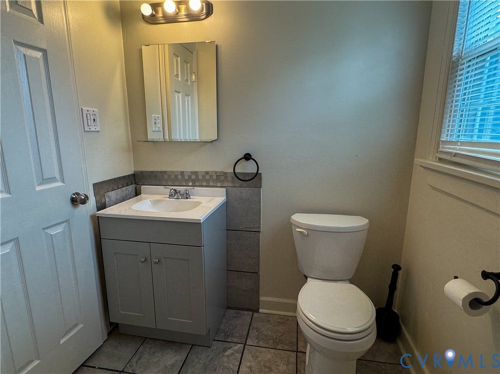 Compact bathroom featuring a contemporary vanity with an integrated sink, a mirrored medicine cabinet, a toilet, and tiled flooring