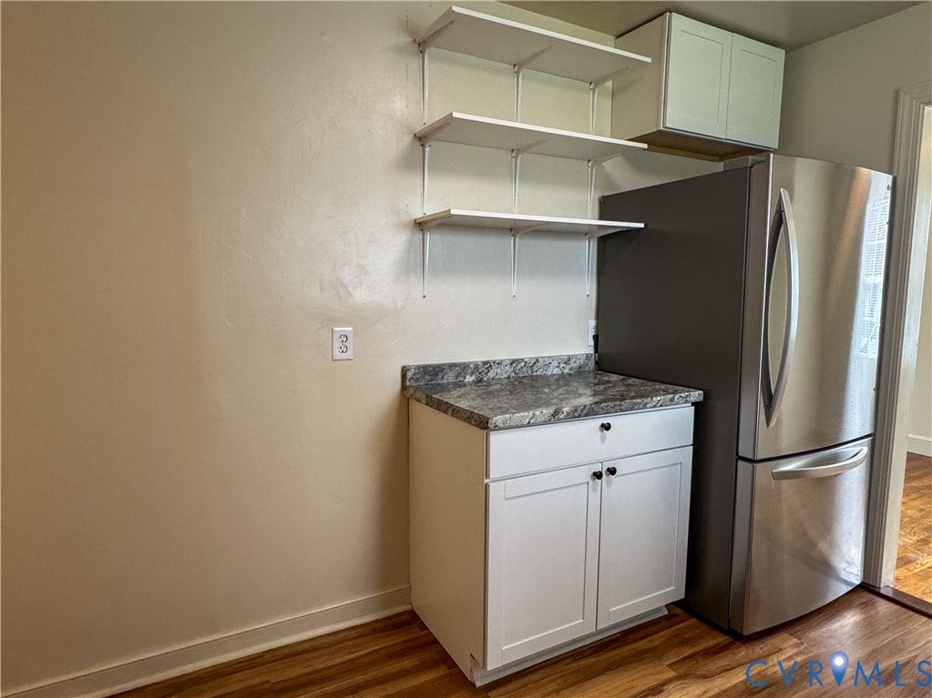 Kitchen area featuring white base cabinetry with black hardware, a grey speckled countertop, and a stainless steel refrigerator