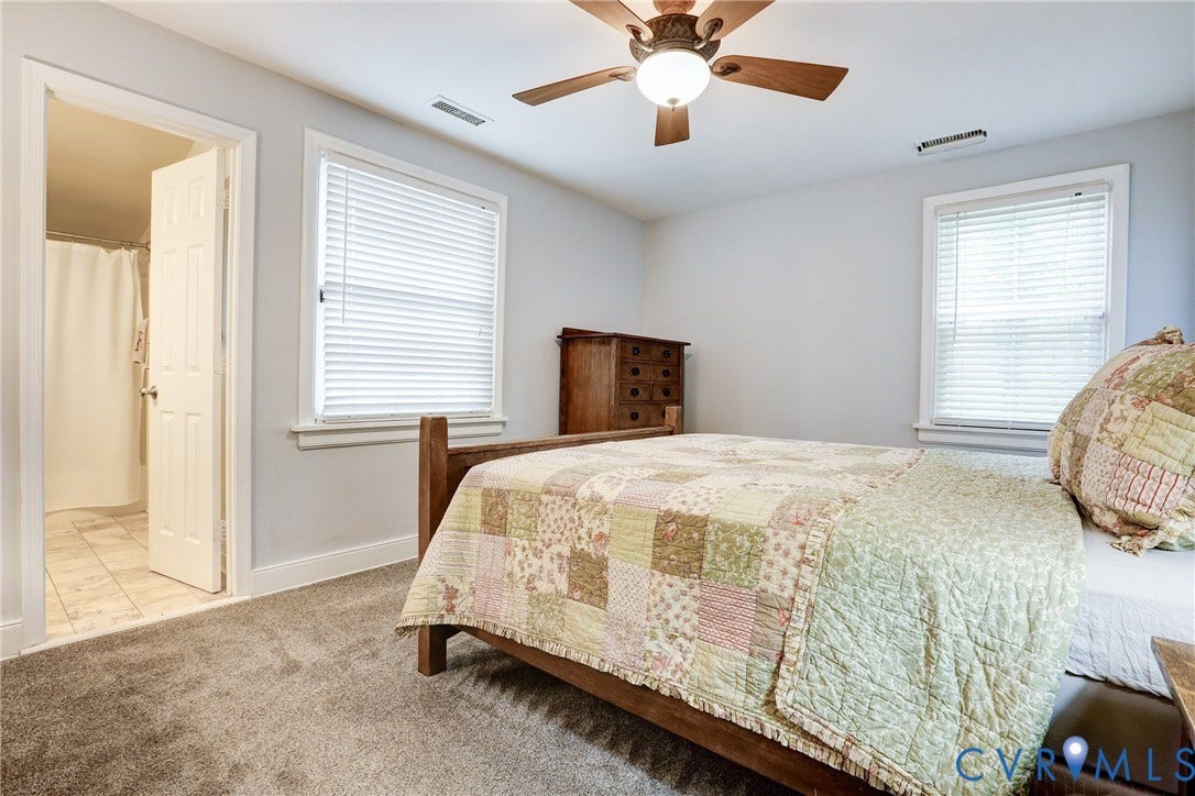 1401 Chowan Road, Henrico, VA 23229 Carpeted bedroom featuring a ceiling fan with light fixture, two windows with blinds, and an adjacent tiled bathroom with a shower