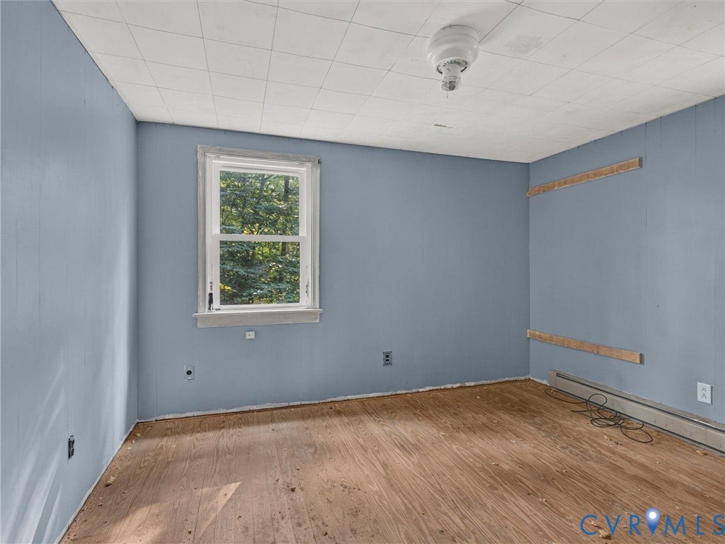 Room featuring wood-finish flooring, a double-hung window, light blue wall finishes, and a ceiling-mounted light fixture