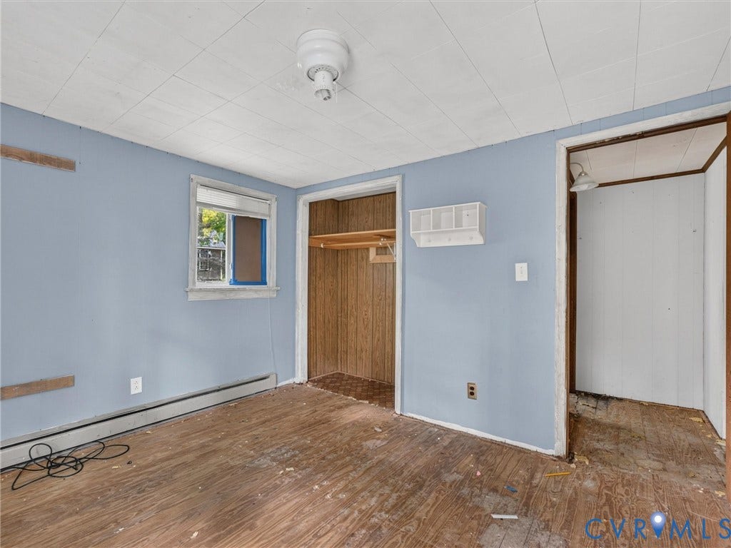 Room featuring light blue walls, wood-finish flooring, a window, and a recessed closet with wood-finish paneling