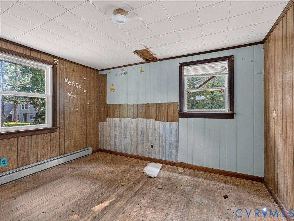 Room featuring wood-finish flooring, paneled wall finishes, and two windows with dark trim