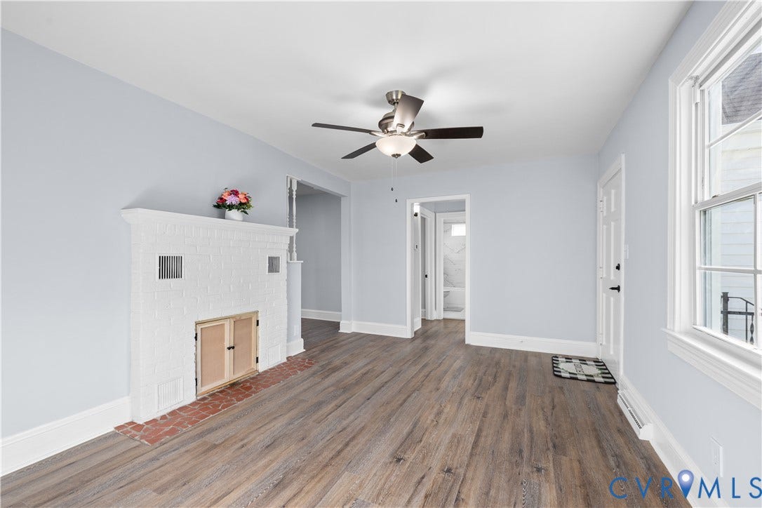 3516 Virginia Street, Woodlawn, Hopewell, VA 23860 Wood-finish flooring throughout, white painted brick fireplace with brick hearth, ceiling fan with integrated lighting, paneled entry door, and double-hung window