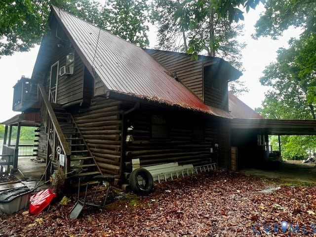 35 Lake Drive, Columbia, VA 23038 Rustic log cabin exterior featuring a red corrugated metal roof, a waterfront location with a visible railing, an exterior wooden staircase, and an attached carport