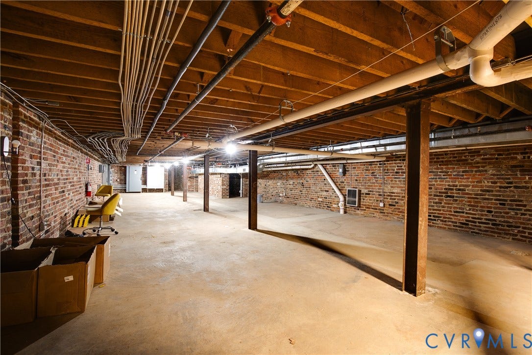 304 E Grace Street, Richmond, VA 23219 Expansive unfinished basement featuring exposed brick walls, concrete flooring, and exposed ceiling joists