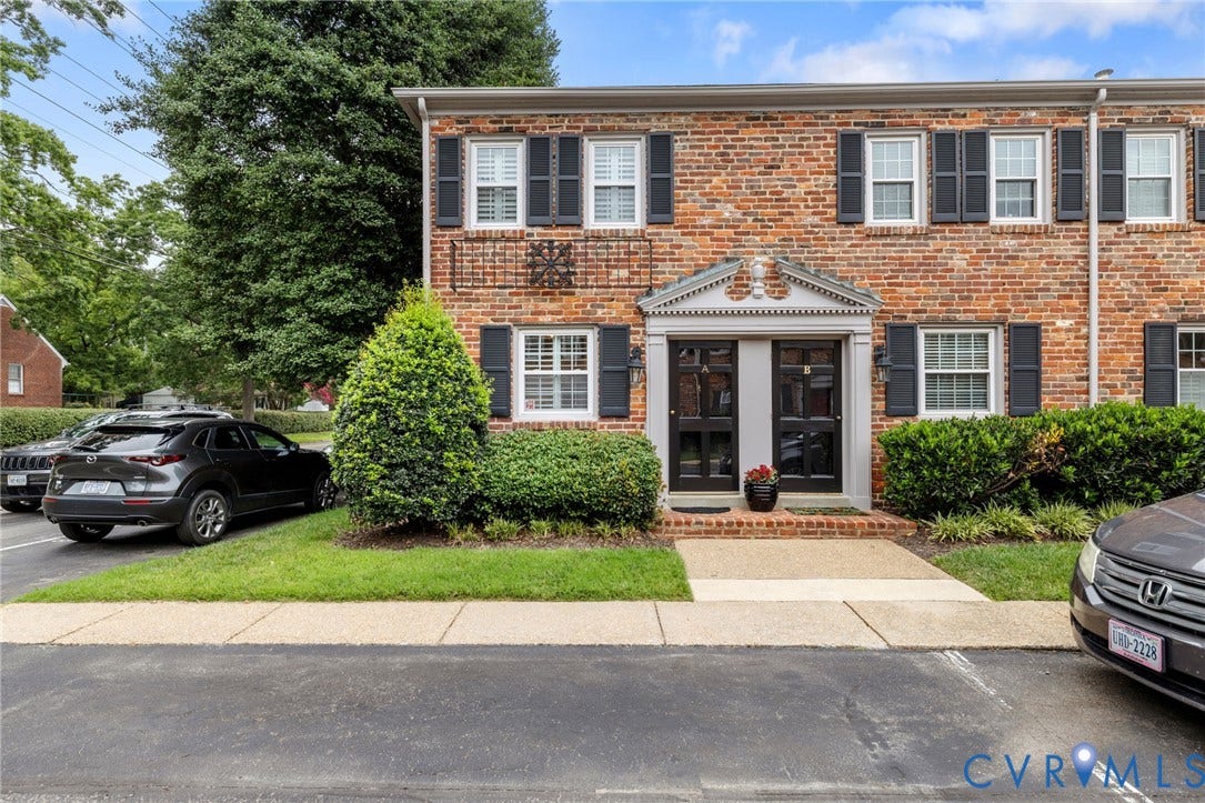 Brick facade townhome featuring black window shutters and a portico entrance