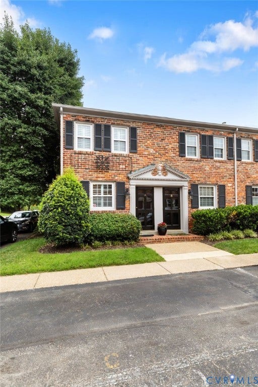 Brick facade building with black window shutters and a structured entryway featuring decorative trim