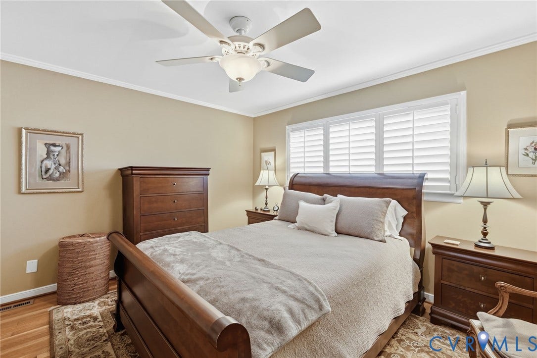 Bedroom featuring wood-finish flooring, crown molding, a ceiling fan with integrated lighting, and plantation shutters