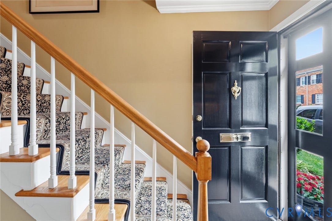 Entryway featuring a paneled black door with brass hardware, wood-finish staircase with white risers and balusters, and a patterned stair runner