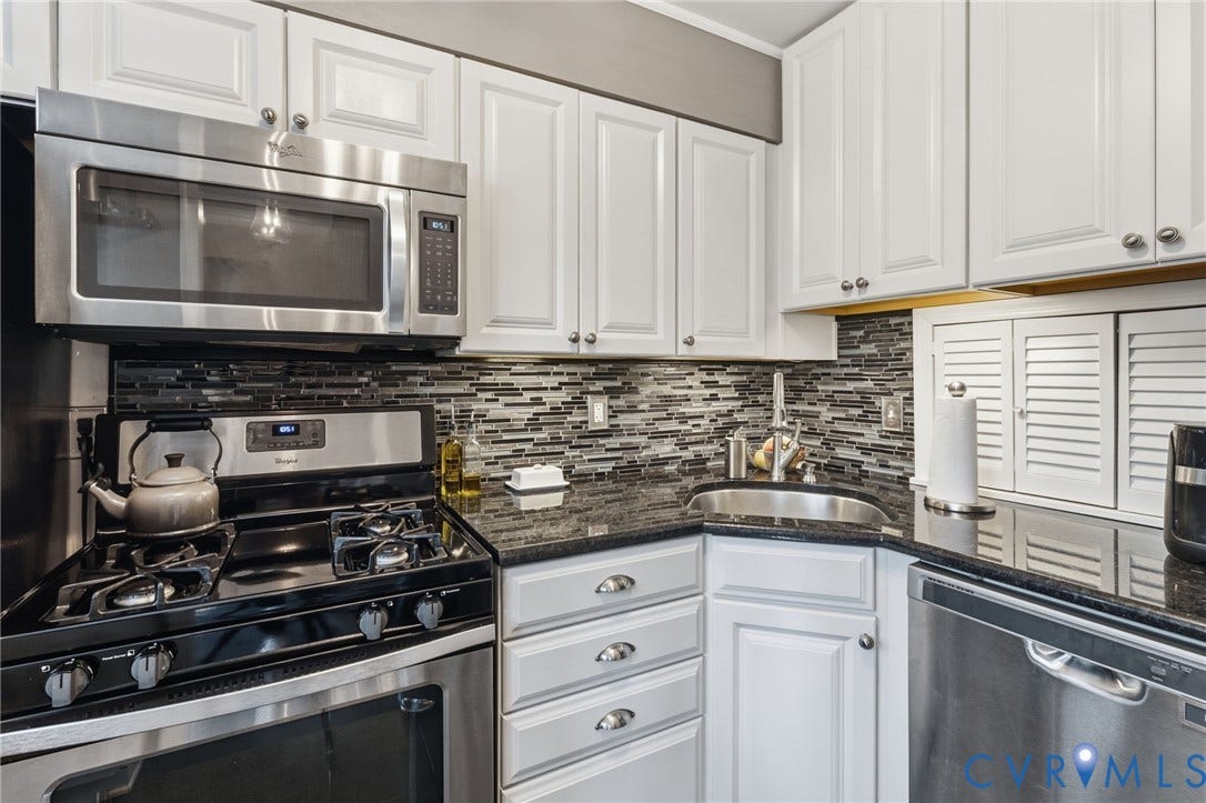 Kitchen featuring white shaker-style cabinetry, black granite countertops, a mosaic tile backsplash, and stainless steel appliances including a gas range and built-in microwave