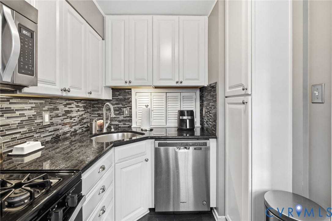 Kitchen featuring white cabinetry, dark stone countertops, a mosaic tile backsplash, and stainless steel appliances including an oven range, microwave, and dishwasher