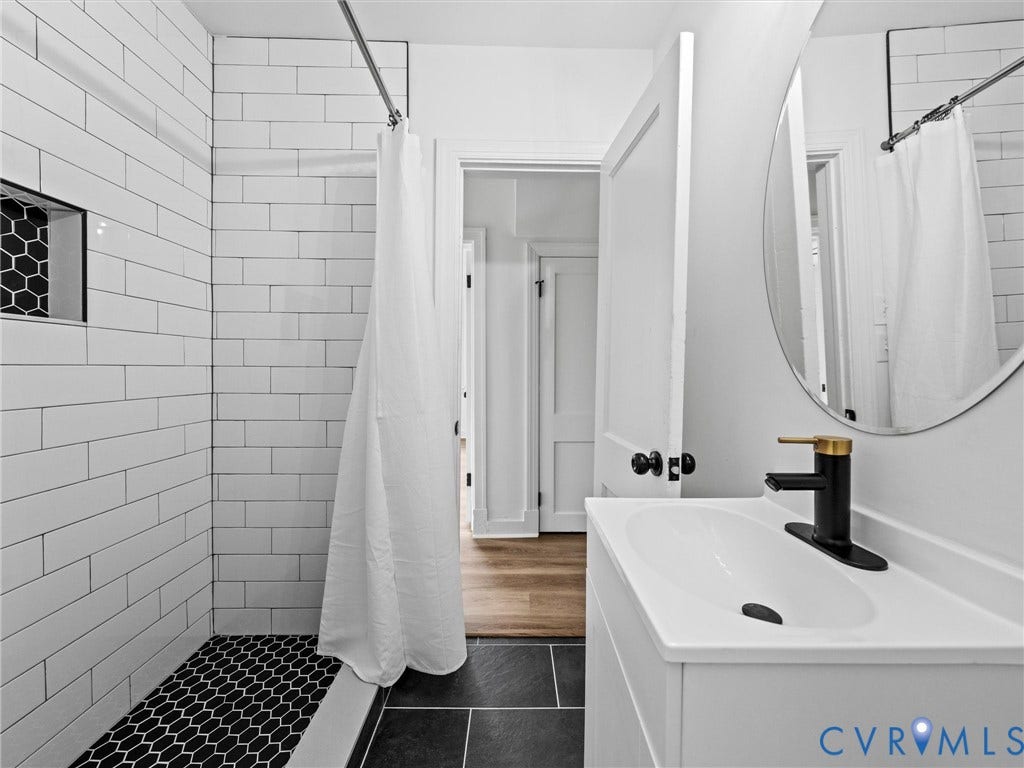 507 Grayson Avenue, Richmond, VA 23222 Bathroom featuring a white subway-tiled shower with black hexagonal floor tiles, a built-in shower niche, a white vanity with integrated sink, and a black and gold single-handle faucet