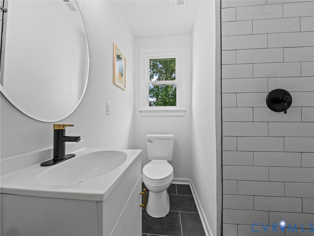 507 Grayson Avenue, Richmond, VA 23222 Bathroom featuring a circular vanity mirror, a modern black and gold faucet, a white vanity with gold hardware, a white toilet, and dark tile flooring