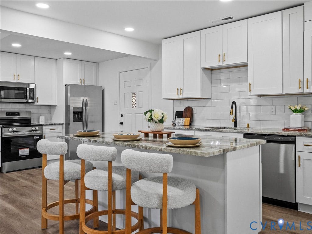 507 Grayson Avenue, Richmond, VA 23222 Kitchen featuring a granite-topped island with seating, stainless steel appliances, white shaker-style cabinetry with gold-tone hardware, and a subway tile backsplash