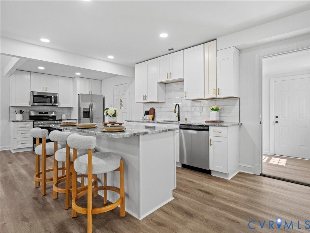 507 Grayson Avenue, Richmond, VA 23222 Modern kitchen featuring an island with stone countertop, white shaker cabinetry with gold-finish hardware, stainless steel appliances, and wood-finish flooring