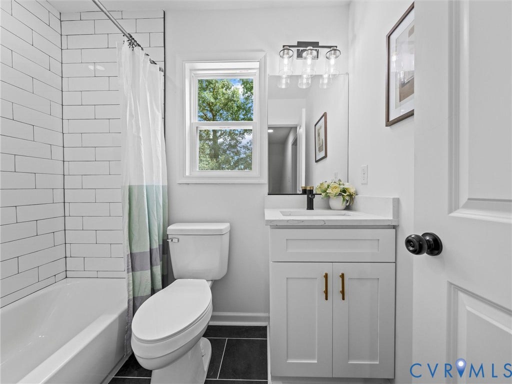 507 Grayson Avenue, Richmond, VA 23222 Bathroom featuring a white subway tile bath/shower surround, a vanity with a white countertop and brass hardware, and dark tile flooring