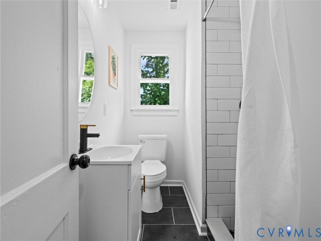 507 Grayson Avenue, Richmond, VA 23222 Bathroom featuring a white vanity with integrated sink, a black and gold-tone faucet, a circular wall mirror, and a toilet with gold-tone hardware