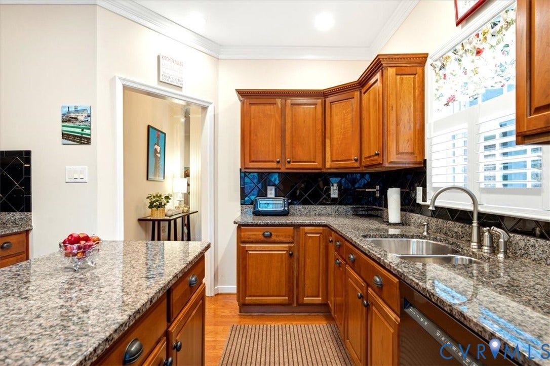 Kitchen featuring granite countertops, wood cabinetry, a stainless steel sink, and white plantation shutters