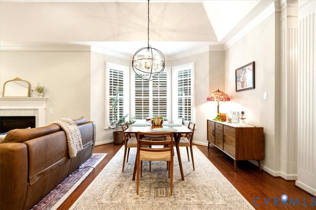 Hardwood flooring, bay window with plantation shutters, fireplace with mantel, recessed ceiling detail, and decorative wall paneling