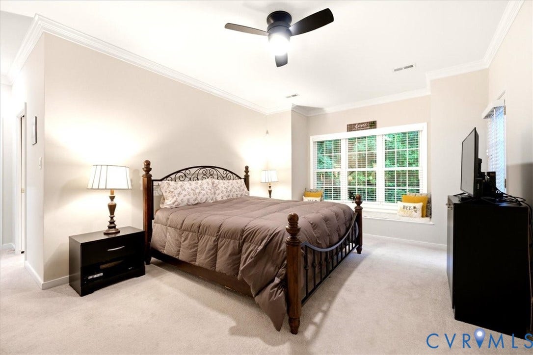 Recessed ceiling with crown molding, ceiling fan, carpeted flooring, and a window seat with a large window