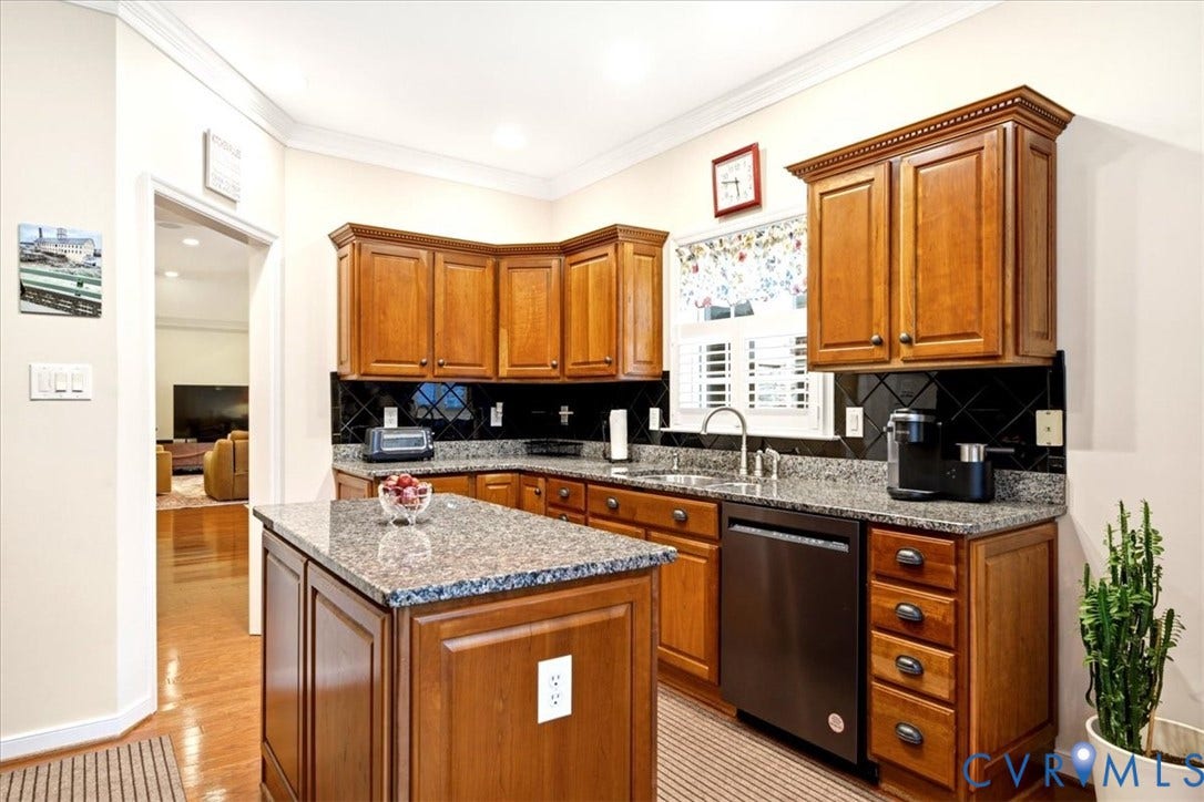 Kitchen featuring wood cabinetry, granite countertops, black tile backsplash, and a central island