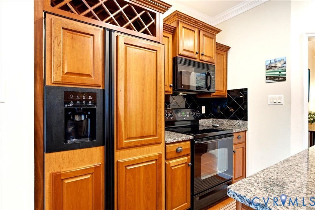 Wood cabinetry, built-in wine rack, black appliances, solid surface countertops, and tiled backsplash